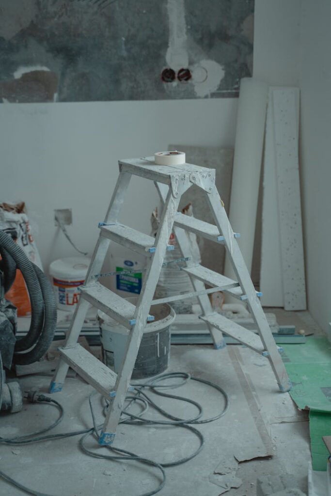pexels-photo-6474121 A metal ladder stands amidst renovation supplies including paints and plaster in an indoor setting.